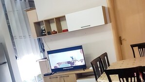Un soggiorno moderno con angolo pranzo, televisione a schermo piatto e angolo cottura con mobili e finestra.
