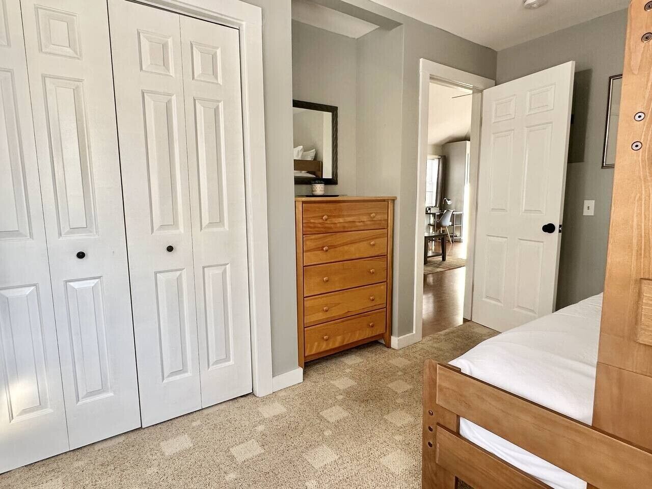 A bedroom with a bed, a wooden dresser, and white double doors.