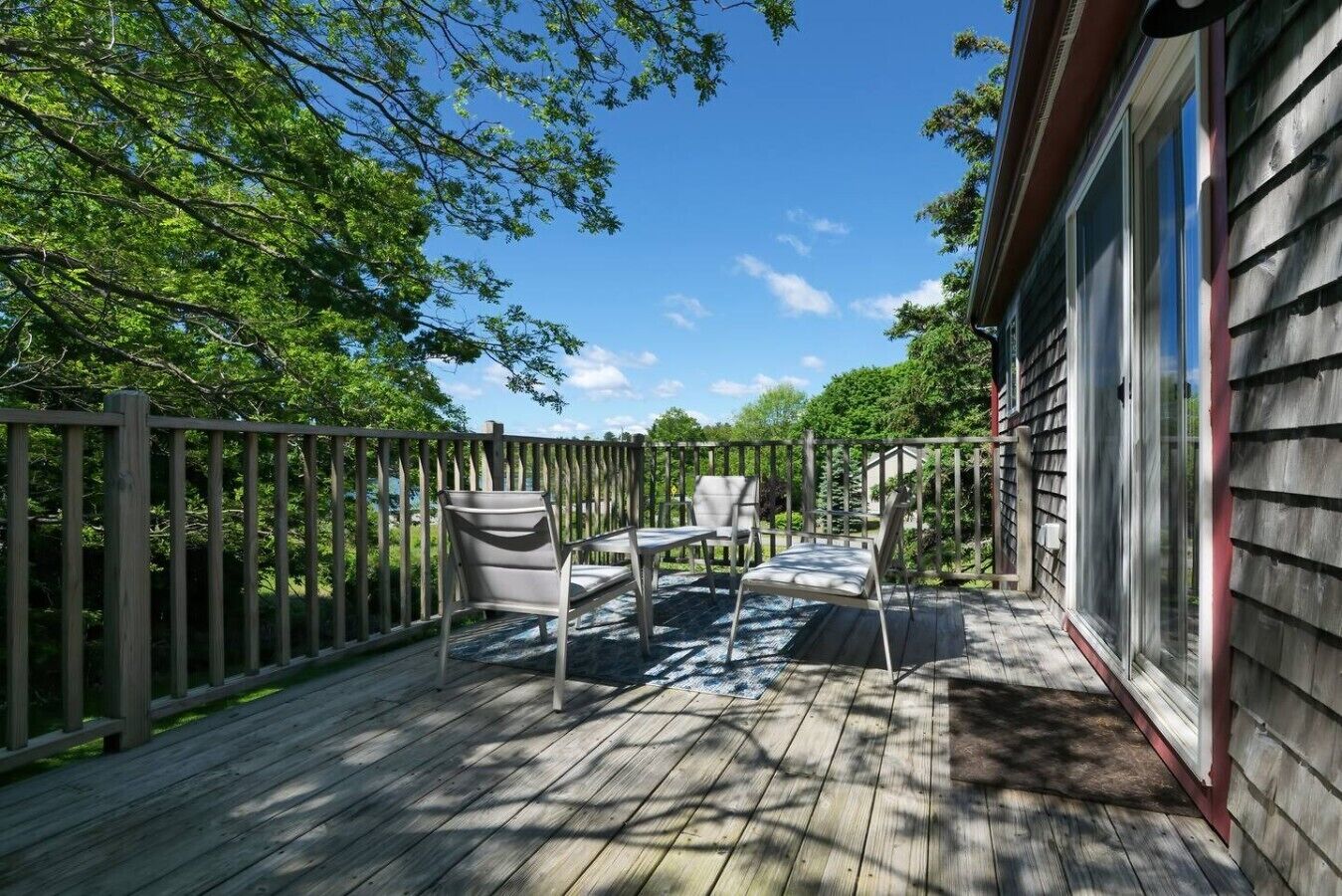 Une terrasse en bois avec des meubles d’extérieur, une vue sur les arbres et un bâtiment doté de grandes fenêtres.