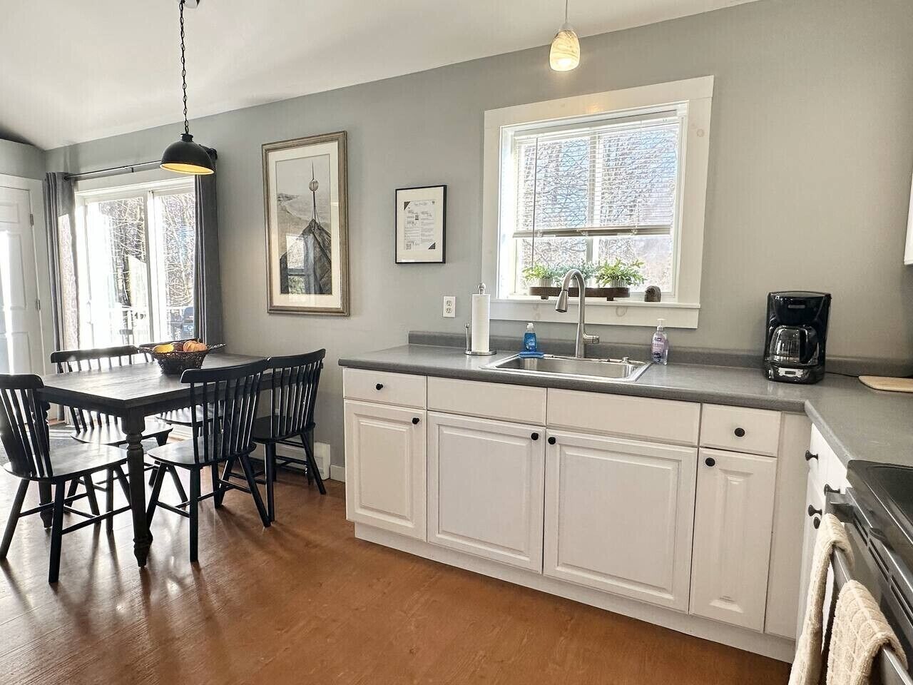 A kitchen with a dining table, chairs, a window with blinds, a hanging light fixture, and a coffee maker.