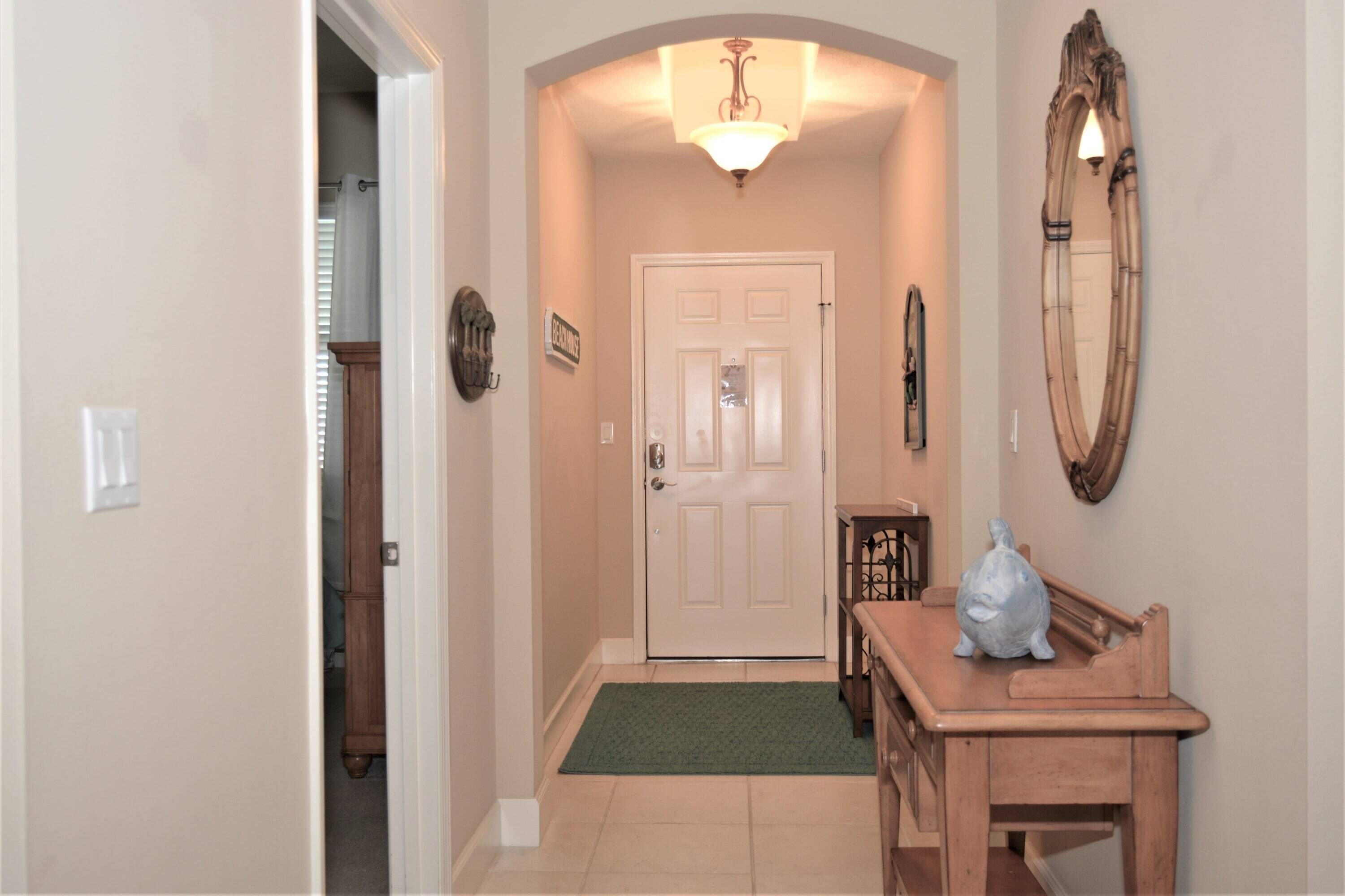 A hallway with a door, a mirror, a light fixture, and a small table with a sculpture.