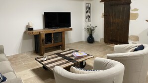 A living room with a wooden coffee table, a TV on a wooden stand, a sofa, and a large wooden door.