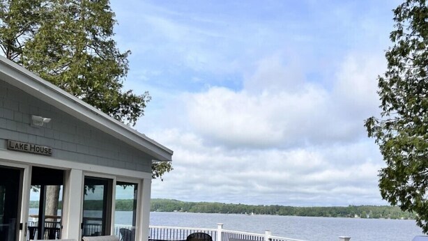 Un espacio de comedor al aire libre con techo y vistas a un lago, una parrilla y un cartel que dice "LAKE HOUSE".