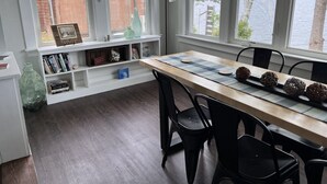 Un comedor con una mesa de madera, sillas negras, un estante blanco con libros y vistas a un lago a través de amplias ventanas.