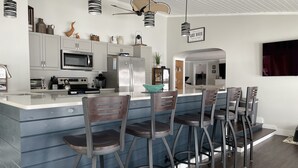 Una cocina moderna con electrodomésticos de acero inoxidable, una barra con taburetes y un ventilador de techo.