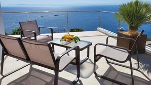 A terrace with a table and chairs, a potted plant, and a view of the sea.