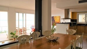 A dining area with a wooden table and chairs, a decorative bowl, and a view of the ocean through large windows.