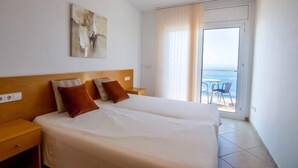 A hotel room with a large bed, a bedside table, a painting on the wall, and a view of the sea through a sliding door.