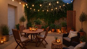 Eine Terrasse im Freien mit einem runden Holztisch und Stühlen, umgeben von Blumentöpfen und Lichterketten.