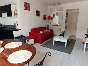 Uma sala de estar moderna com um sofá vermelho, uma mesa de centro branca e uma mesa de jantar de madeira com jogos americanos trançados.