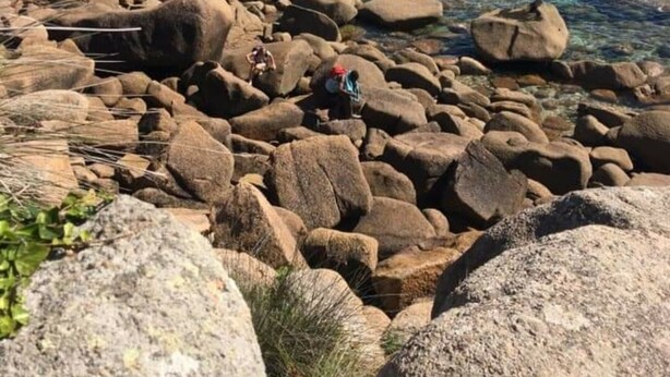 Ein felsiger Strand mit klarem Wasser und Booten in der Ferne.