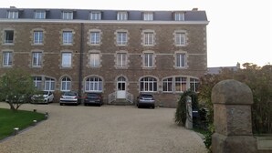 Ein mehrstöckiges Steinhaus mit Kiesweg und geparkten Autos.