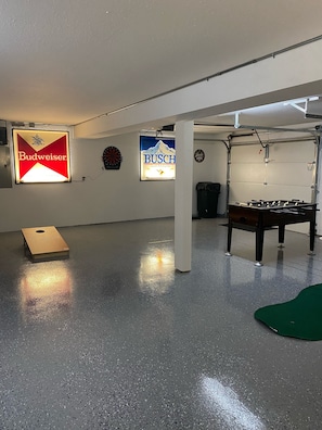 Une pièce avec un jeu de fléchettes, un baby-foot et des panneaux publicitaires pour les bières Budweiser et Busch.