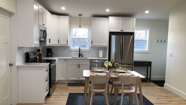 A modern kitchen with white cabinets, a stainless steel refrigerator, and a dining area with a table set for four. - Bright new 2nd-floor space near Mayo Clinic & downtown (Rochester)