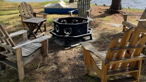 Ein Sitzbereich am Seeufer mit Adirondack-Stühlen und einer Feuerstelle.