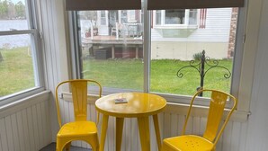 Ein Eckzimmer mit Fenster, zwei gelbe Stühle und einem kleinen runden Tisch.