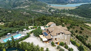 A stone building with a pool and outdoor seating, surrounded by greenery and a mountainous backdrop.