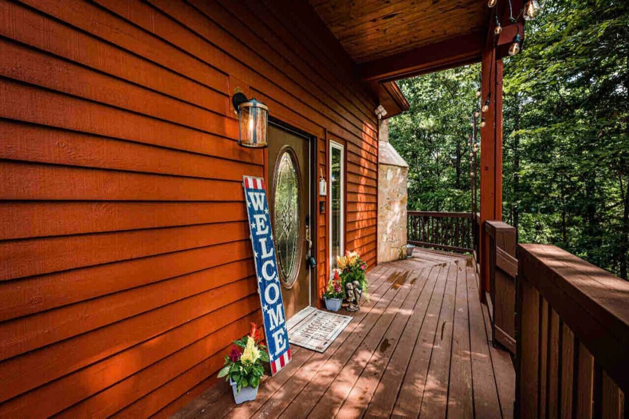 Une cabane en bois avec une véranda, une pancarte de bienvenue et une boîte aux lettres.