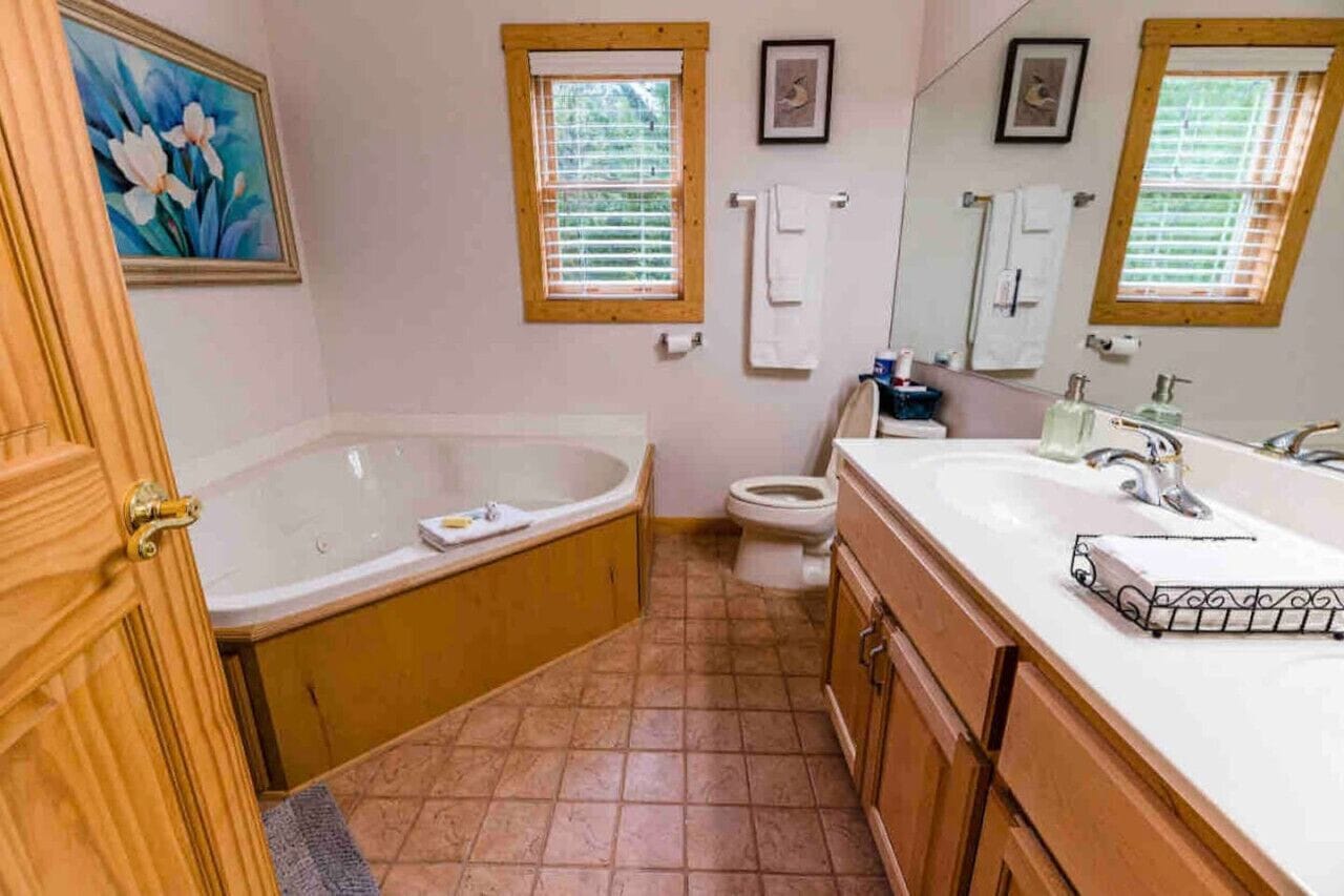 Un baño con bañera, inodoro y lavabo. Hay armarios de madera y un espejo grande sobre el lavabo.