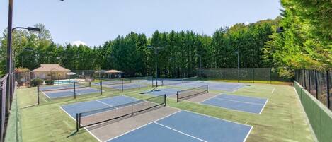 A tennis court complex with multiple courts, a covered seating area, and a street lamp.