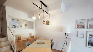 Cocina moderna con una mesa de madera, luces colgantes y una escalera que sube a otro nivel.