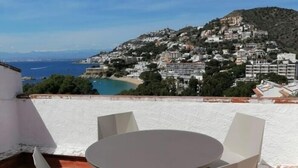 Una terraza con una mesa redonda y cuatro sillas, con vistas a un pueblo costero con edificios en una colina y una playa al fondo.