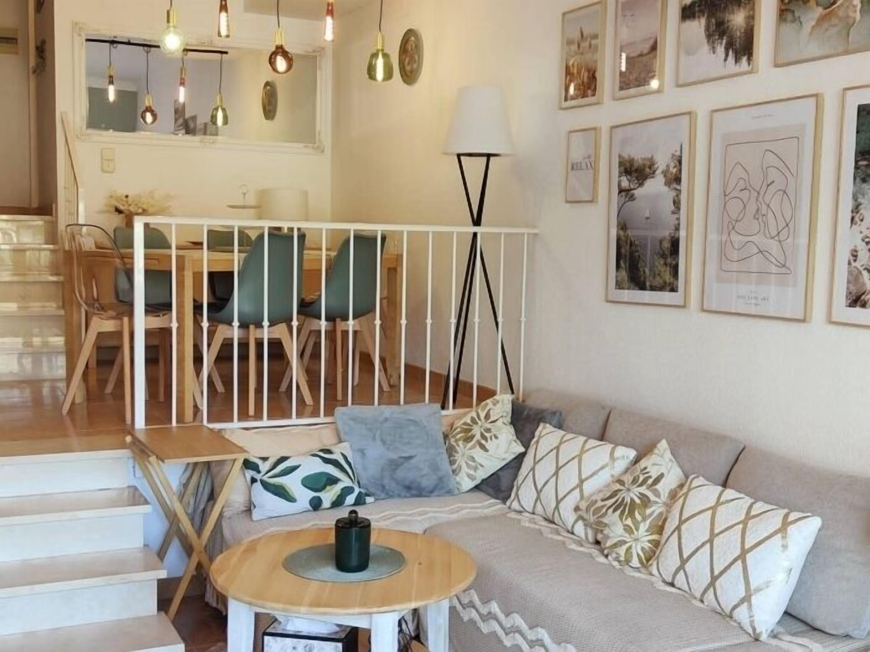 A modern living room with a staircase, a dining area, and artwork on the walls.