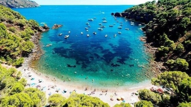 Una playa costera con aguas turquesas cristalinas, embarcaciones y vegetación.