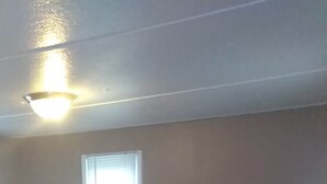 Ein Zimmer mit schrägem Dach, einem Fenster mit Jalousien und einem Lüftungsgitter am Boden.