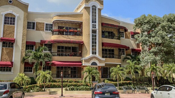 Hotel com vários andares, varandas, toldos vermelhos e palmeiras.