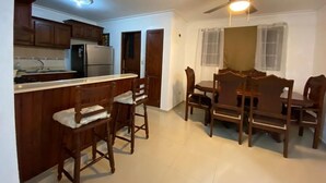 Uma cozinha com armários de madeira, uma geladeira, uma mesa de jantar com cadeiras e um ventilador de teto.