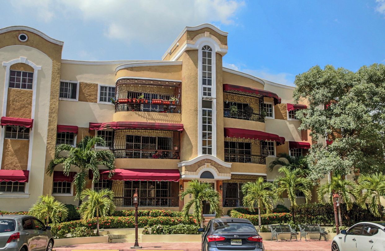 A multi-story hotel with balconies, red awnings, and palm trees.