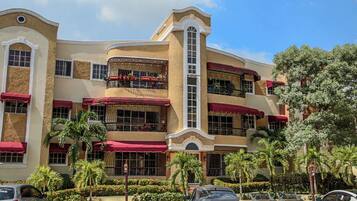 Un hotel de varios pisos con balcones, toldos rojos y palmeras.