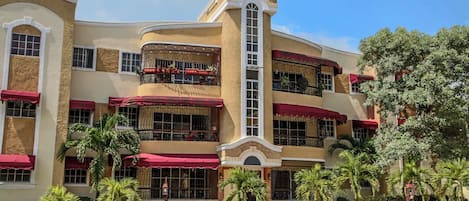 A multi-story hotel with balconies, red awnings, and palm trees.