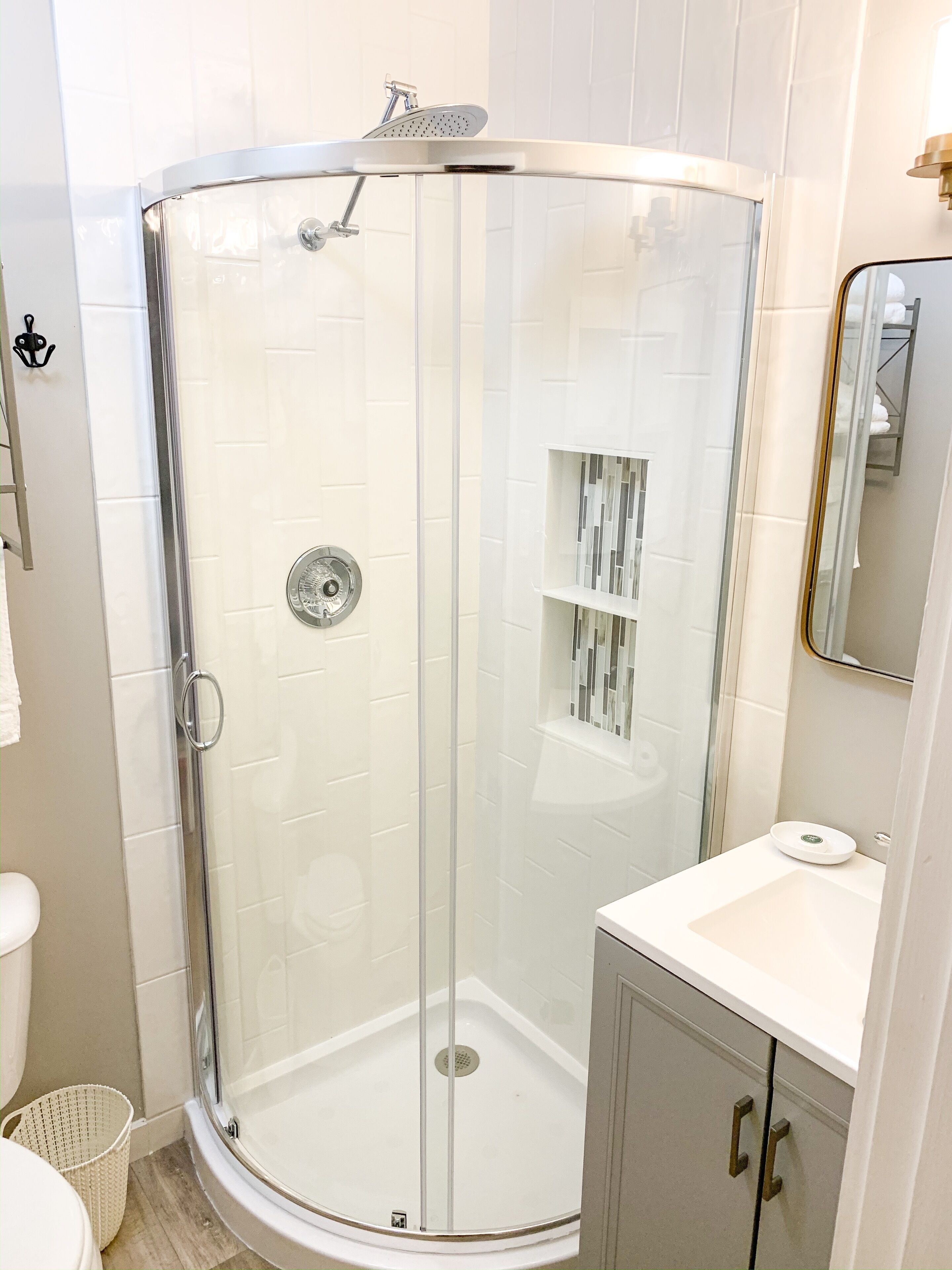 A modern bathroom with a glass-enclosed shower, white tiles, a white sink, and a mirrored cabinet.