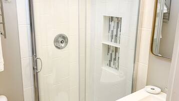 A modern bathroom with a glass-enclosed shower, white tiles, a white sink, and a mirrored cabinet.