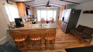 A compact kitchen with a central island, wooden chairs, a refrigerator, and a dining area with chairs. - Topsy's Trailer, Private, FAST WiFi, Small Dog Ok, HOT TUB, Close to AVL/Hendo (Arden)