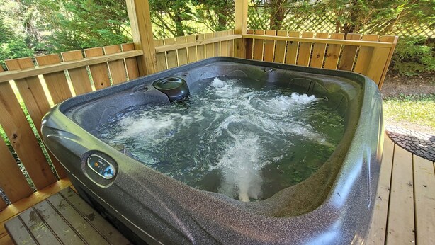 A hot tub on a wooden deck with a wooden fence and greenery in the background. - Topsy's Trailer, Private, FAST WiFi, Small Dog Ok, HOT TUB, Close to AVL/Hendo (Arden)