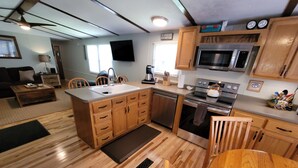 A modern kitchen with wooden cabinets, a stainless steel microwave, and an oven. There is a dining area with a wooden table and chairs. - Topsy's Trailer, Private, FAST WiFi, Small Dog Ok, HOT TUB, Close to AVL/Hendo (Arden)