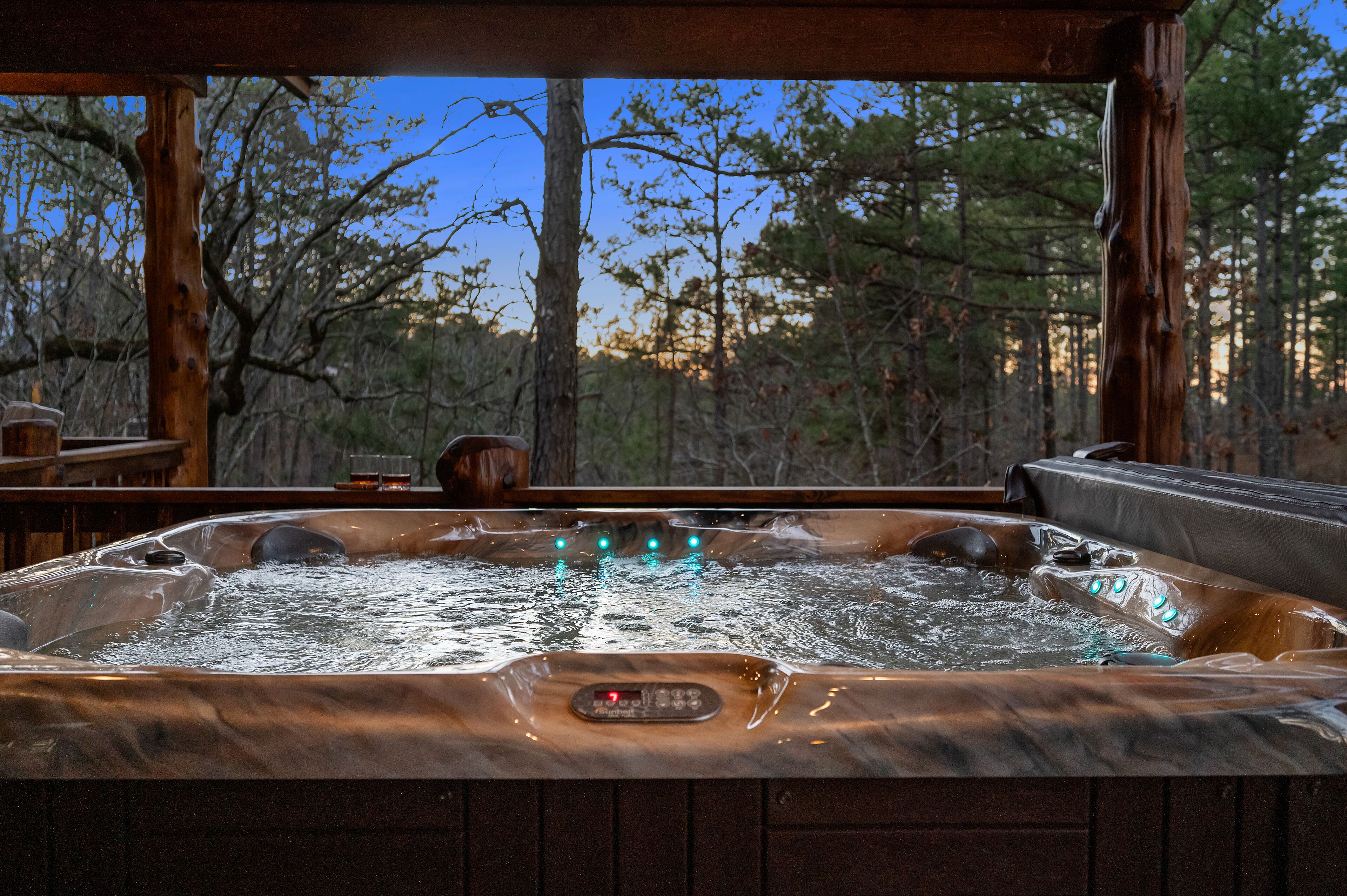 A hot tub with a control panel, set in a wooden cabin with a view of trees and a clear sky.