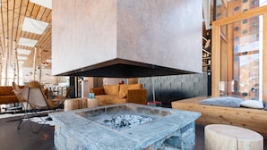 A modern interior with a stone fire pit, wooden furniture, and a high ceiling with exposed beams. - Timberlodge (Oz)