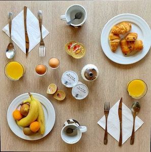 Une table en bois dressée pour le petit-déjeuner, avec des croissants, des œufs, des bananes et du jus.