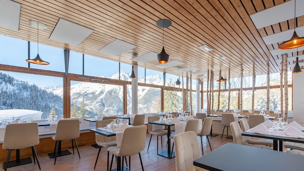 A restaurant with wooden ceiling and large windows offering mountain views. Tables are set with chairs and dining ware. - Timberlodge (Oz)