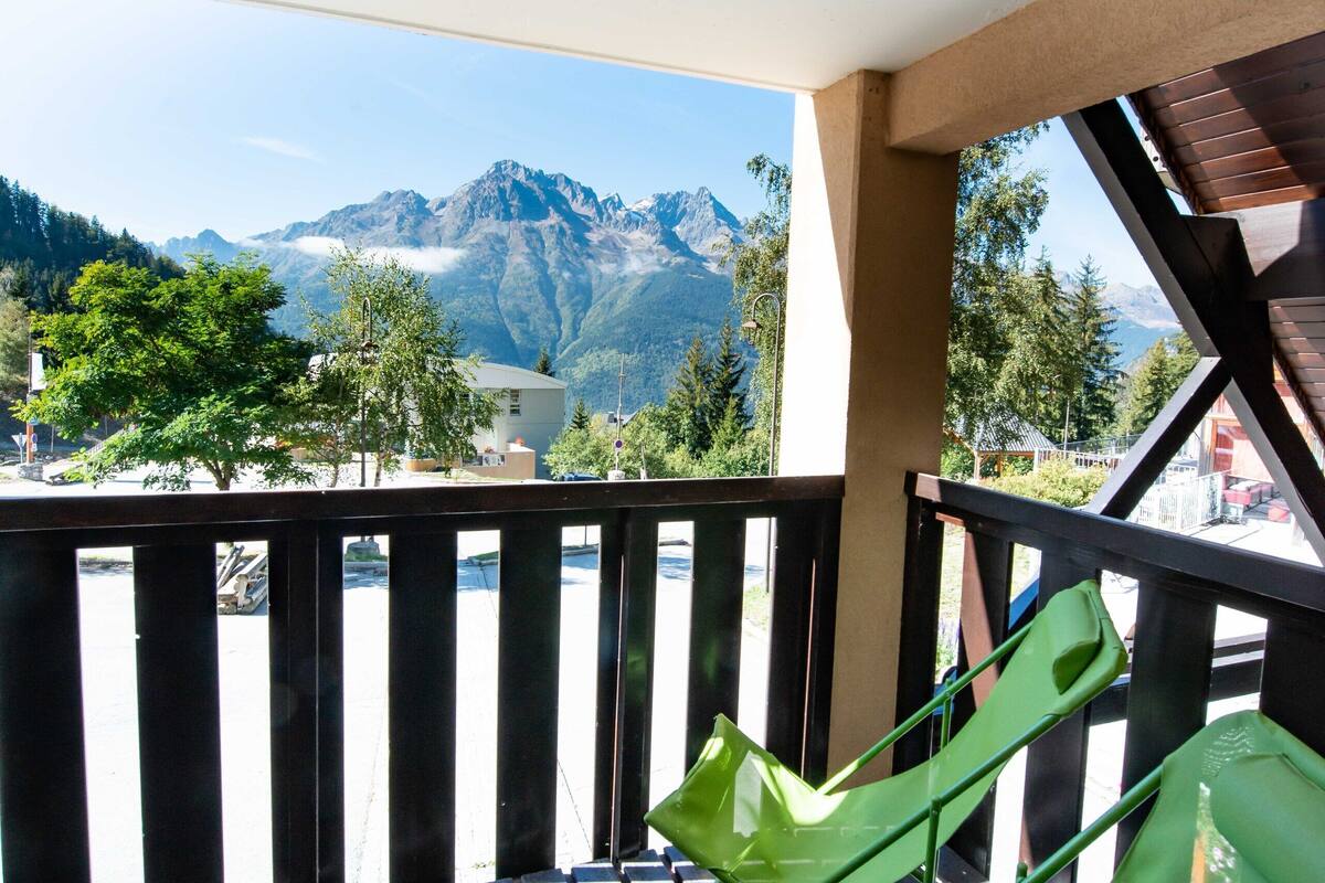 A balcony with a view of mountains, a wooden table, and a green chair.