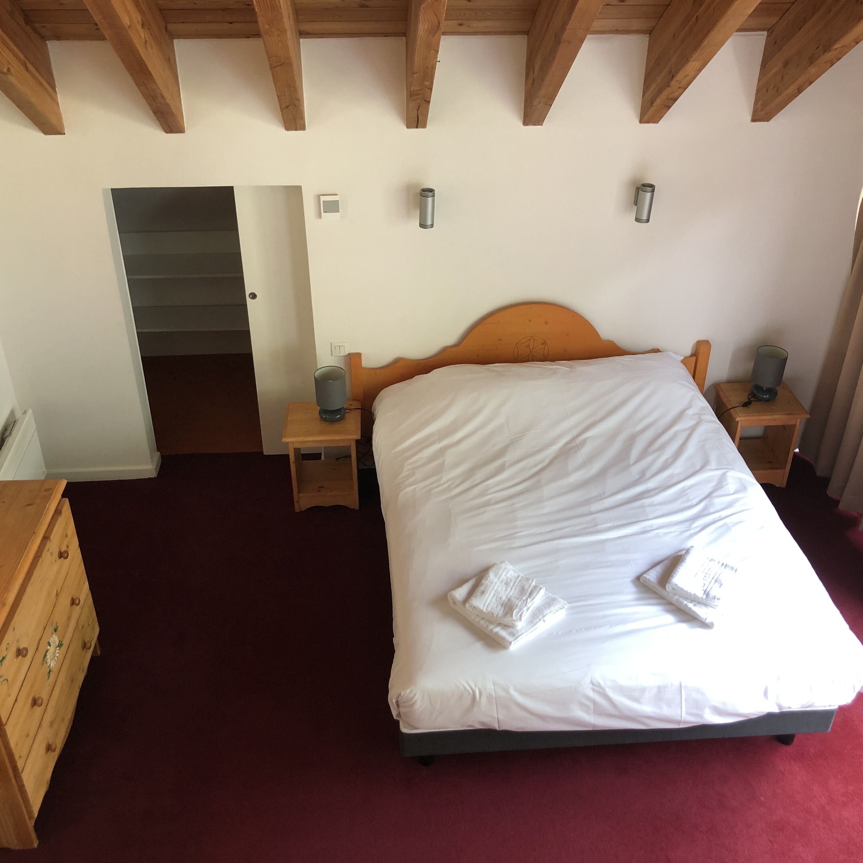 Ein Schlafzimmer mit einem hölzernen Bett, zwei Nachttischen, einer Kommode und einer Tür zu einem weiteren Raum.