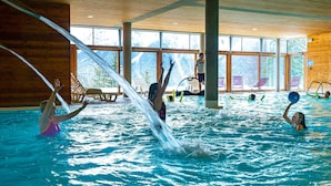 An indoor swimming pool with clear views of mountains through large windows, wooden beams on the ceiling, and several lounge chairs around the pool area. - Timberlodge (Oz)