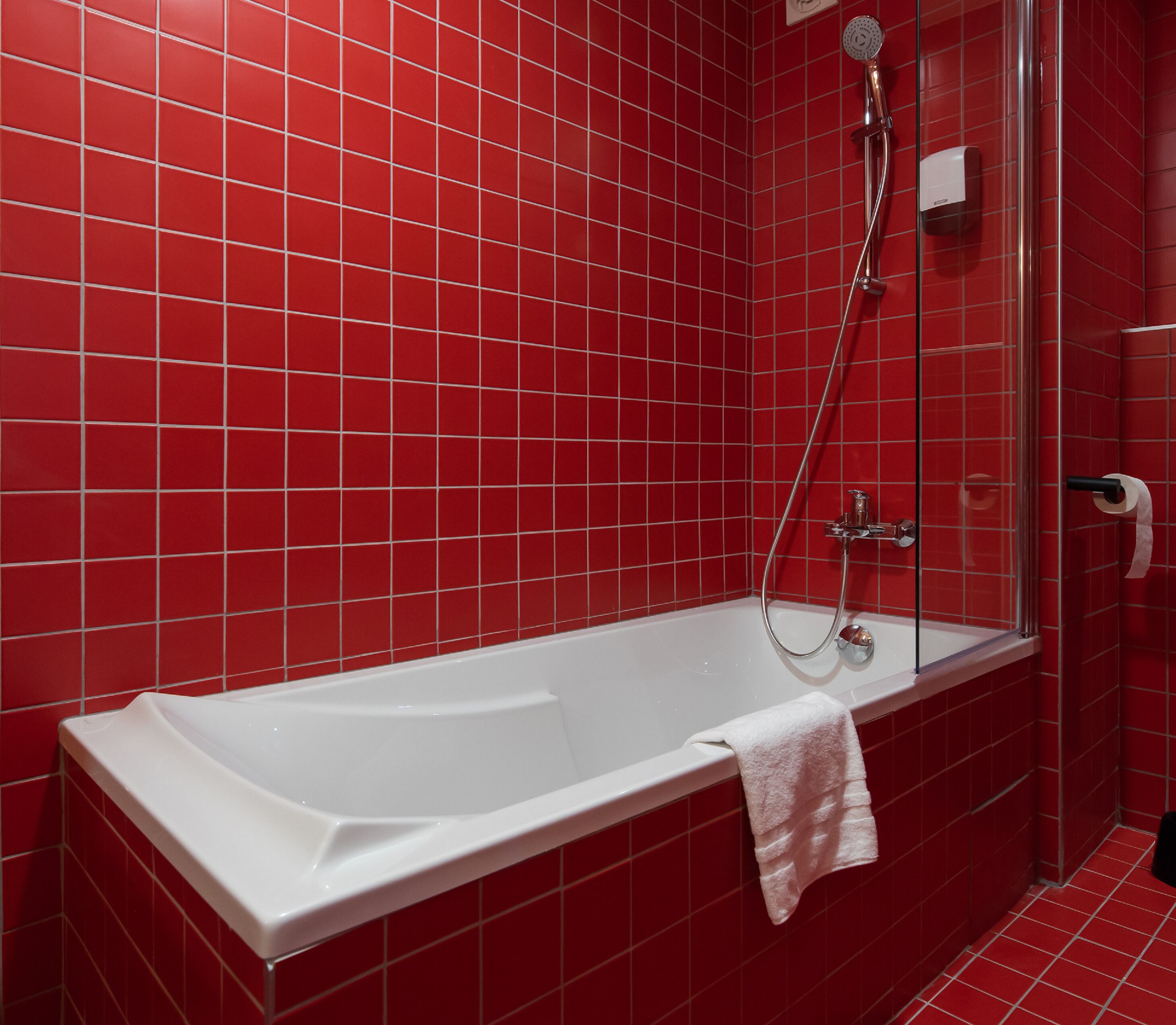 A modern bathroom with a white bathtub, red tiled walls, and a glass shower enclosure.