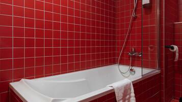 A modern bathroom with a white bathtub, red tiled walls, and a glass shower enclosure.