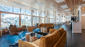A spacious lounge area with a large window offering a mountain view, a wooden ceiling, and modern furniture. - Timberlodge (Oz)