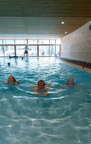 Une piscine intérieure à l’eau claire, avec des murs en bois et de grandes fenêtres.